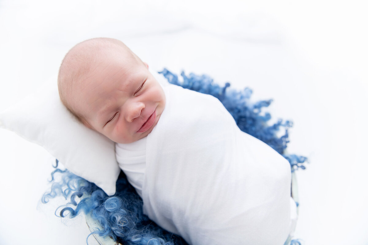 A newborn baby sleeps in a bucket with a blue blanket posed by an Atlanta newborn photographer