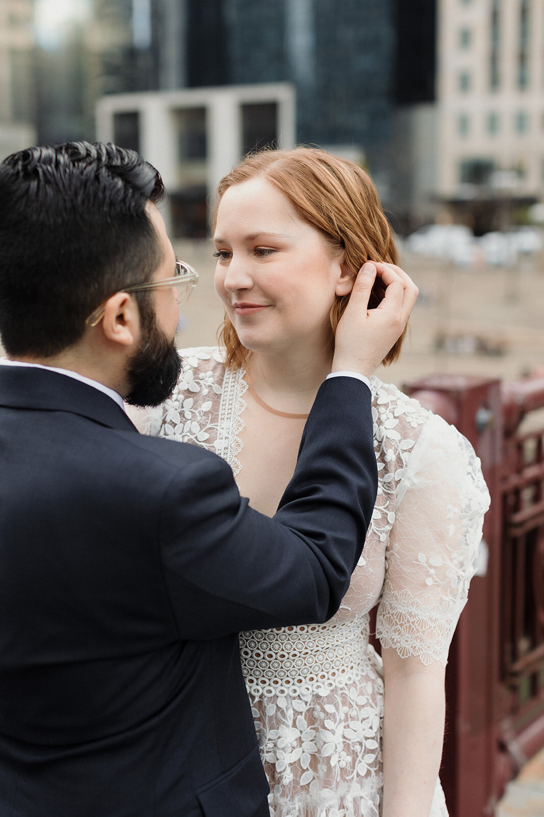 Wedding couple standing on Chicago River bridge smiling at each other. Groom is tucking bride's hair behind her ear.