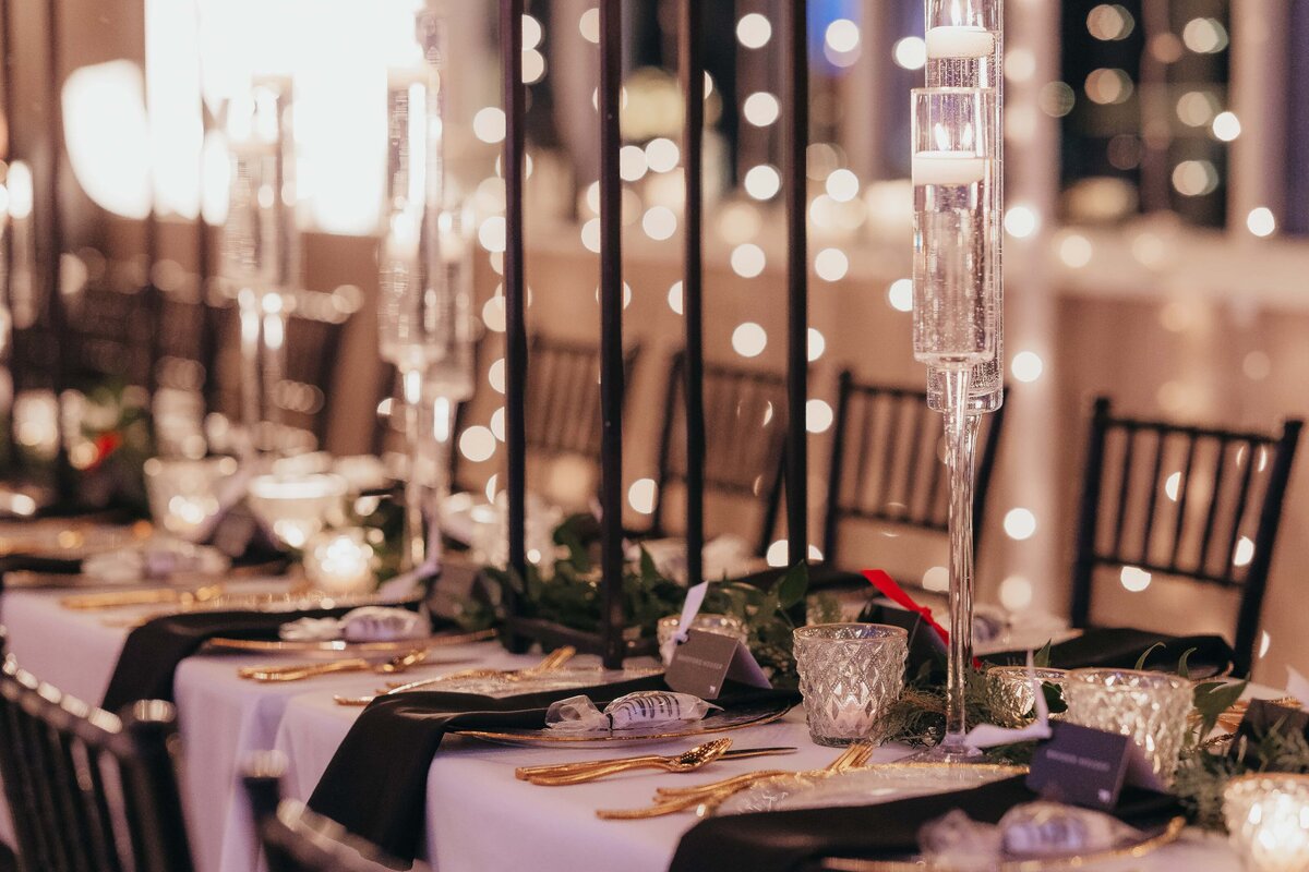 Elegant banquet table set for an event with tall crystal candle holders, gold plates, and twinkling background lights, ideal for park farm winery weddings.