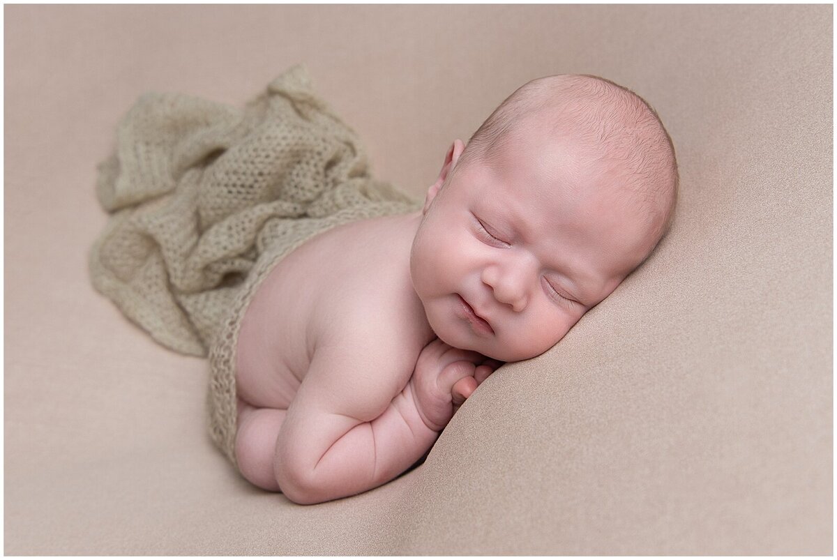 Naked baby boy sleeping on a tan blanket and  covered partly with a sage textured blanket.