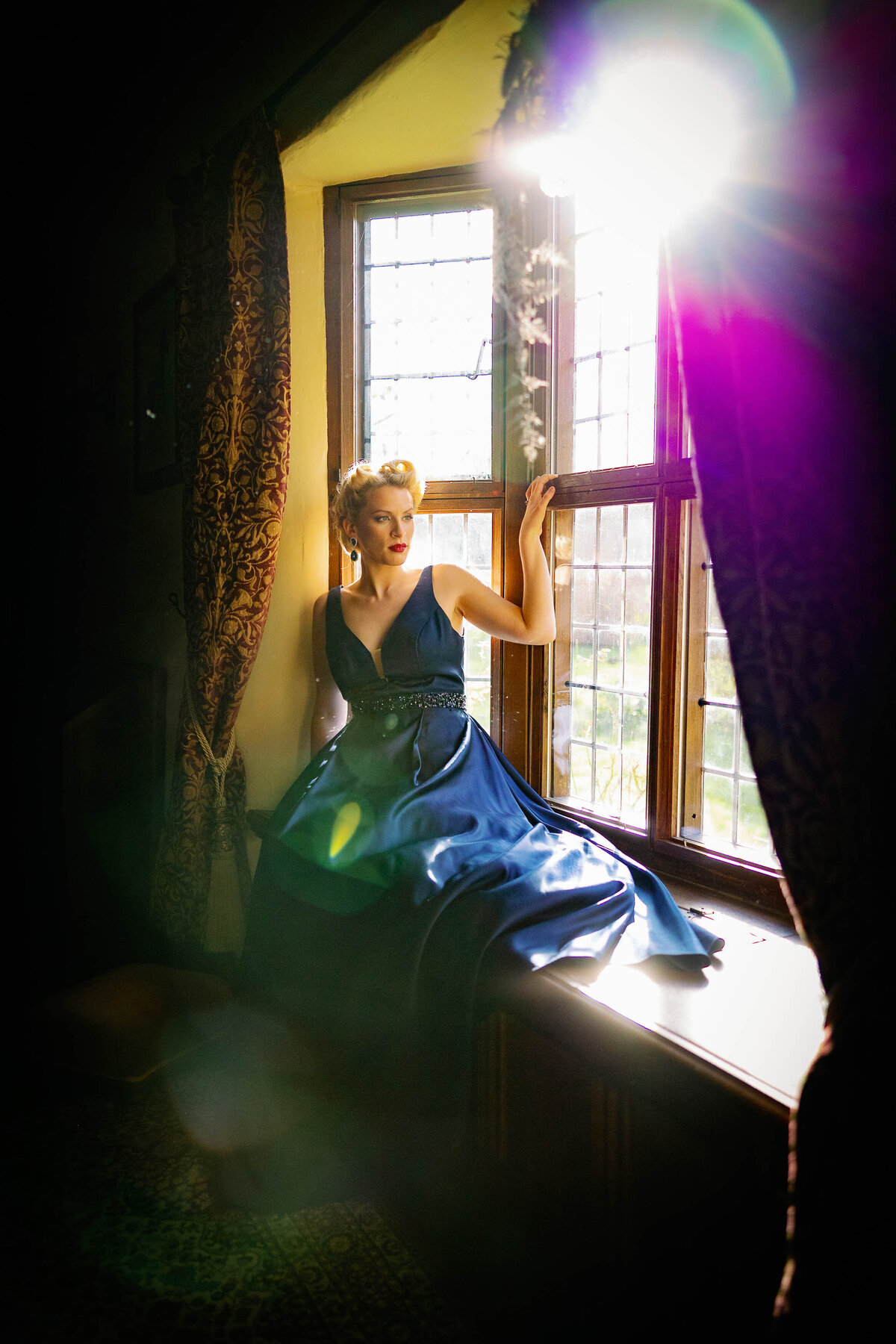 Bride wearing a blue dress sat in the window of home as the sunshine pours through the windows