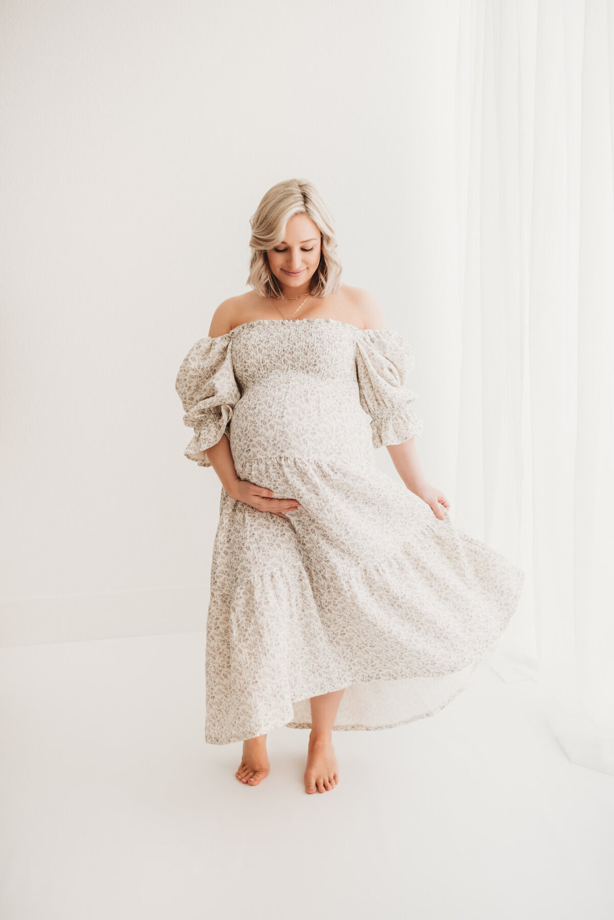 pregnant woman swishing her dress in white studio photo room