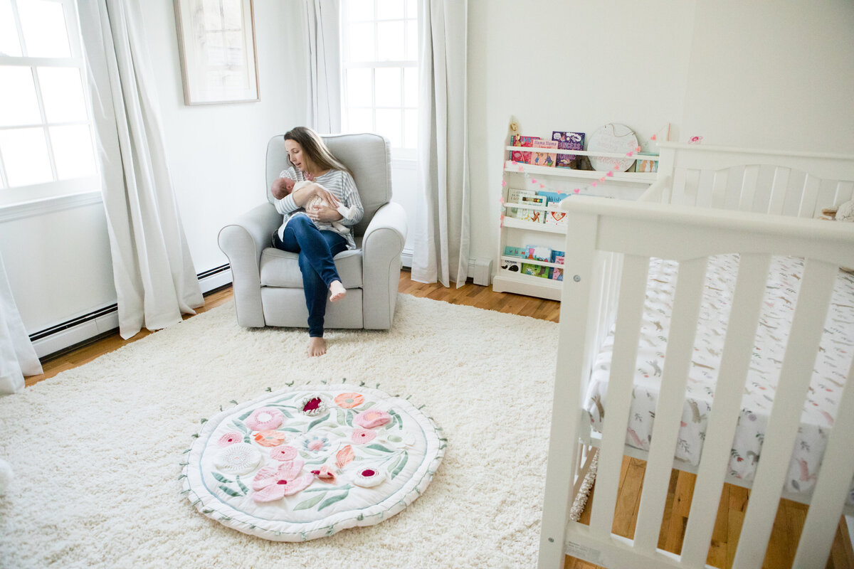 Wide shot of a nursery white mother holding her baby in a glider New City newborn photographer Milestone Images