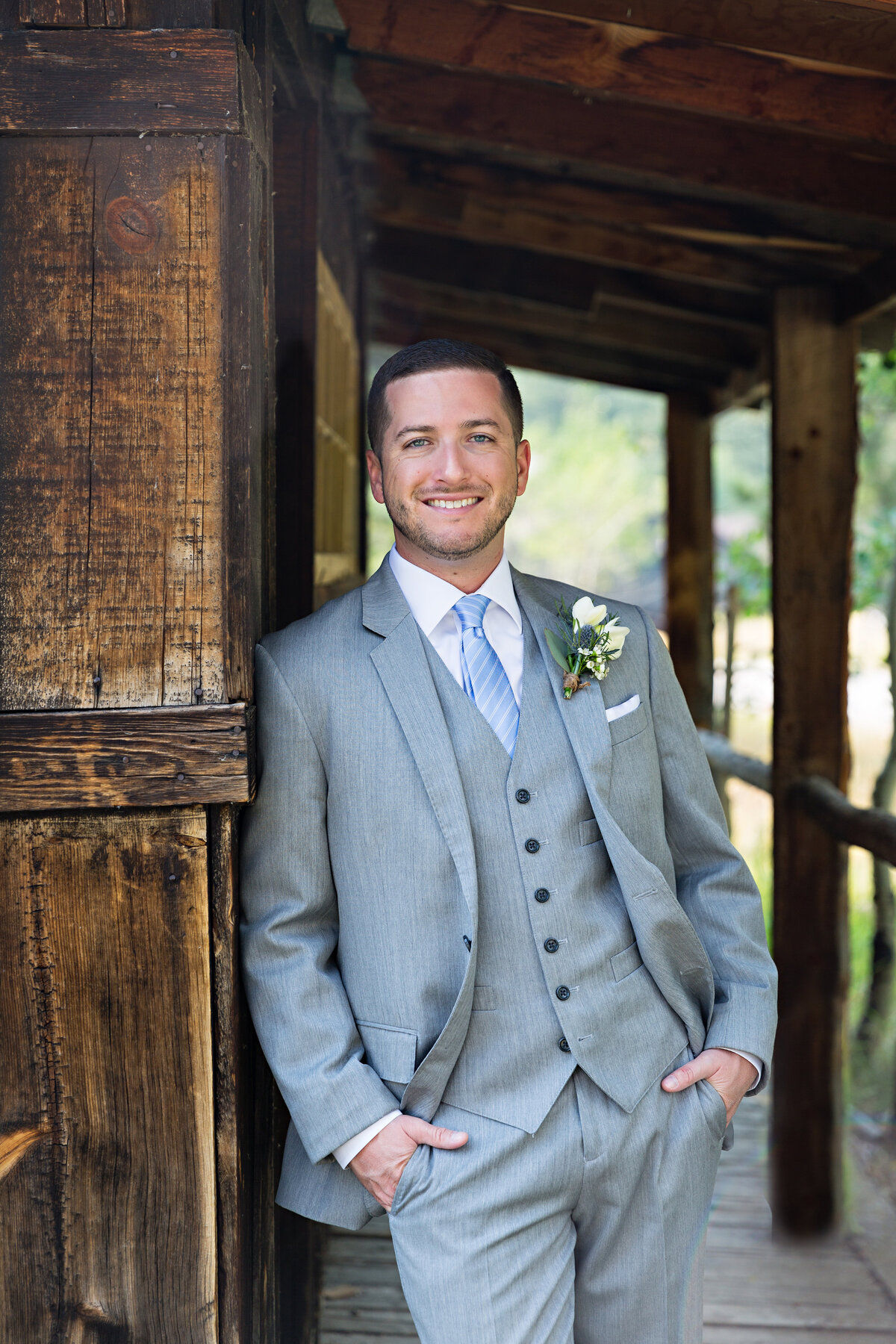 groom in gray suit leans on a barn wall