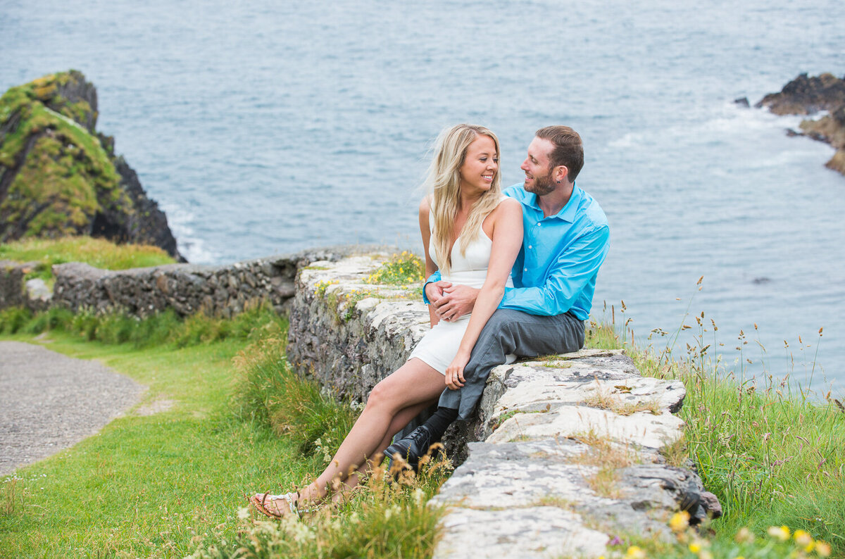 Engagement portrait of young couple sitting on a natural stone wall in Dunquin