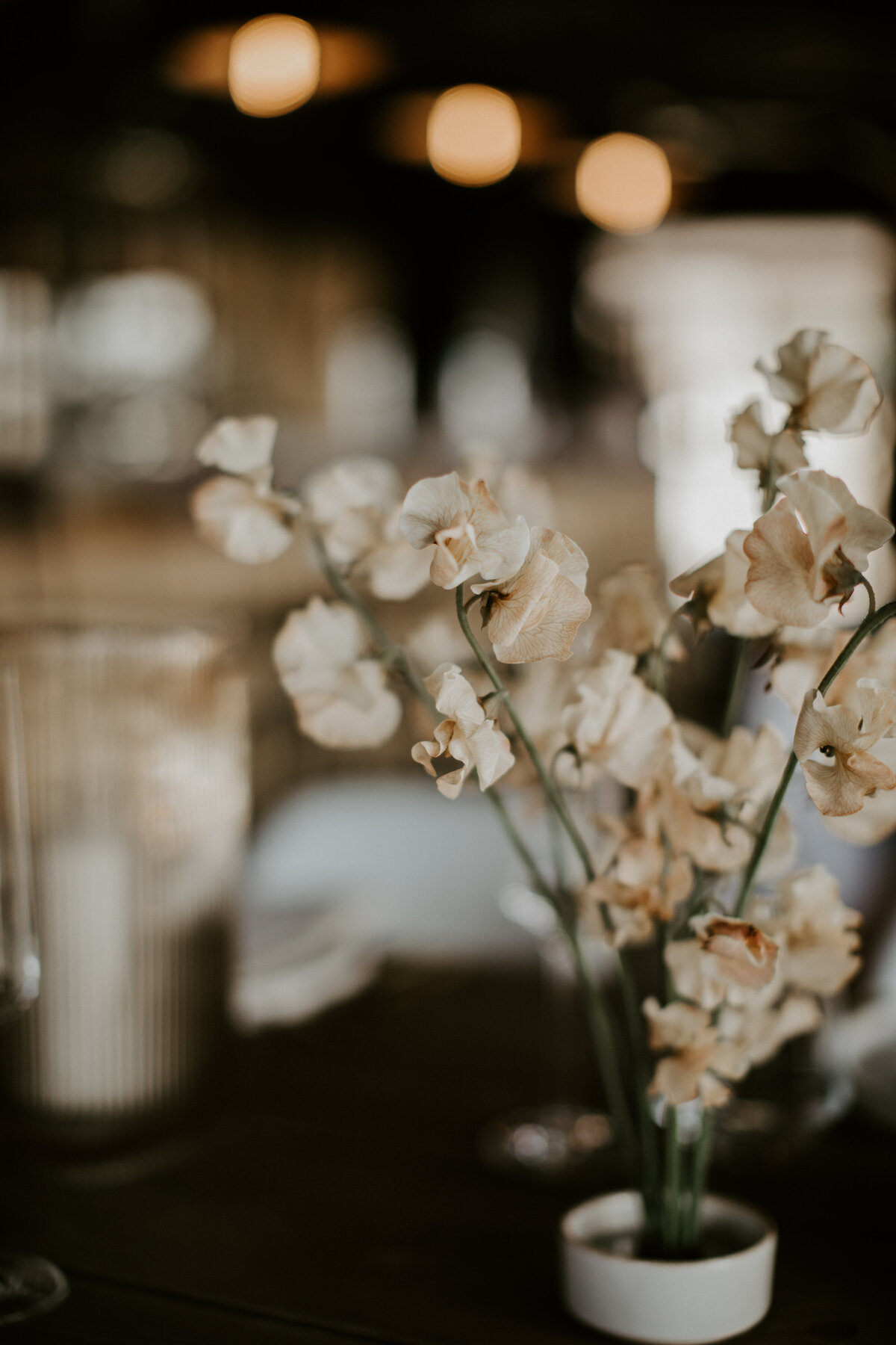 Ivory-colored flowers set on a table with candlesticks in  glass .