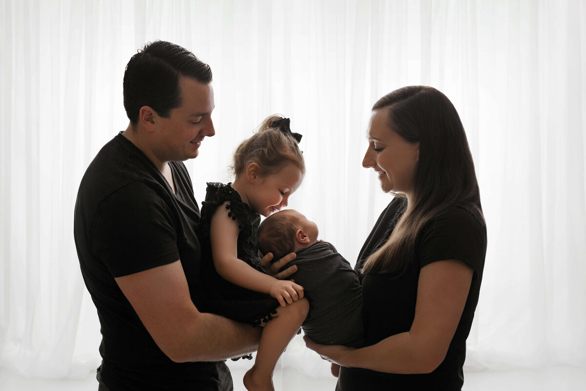 pregnant mother in a black dress standing on front of a white curtain at a maternity photography session with a photographer at a northern virginia photography studio