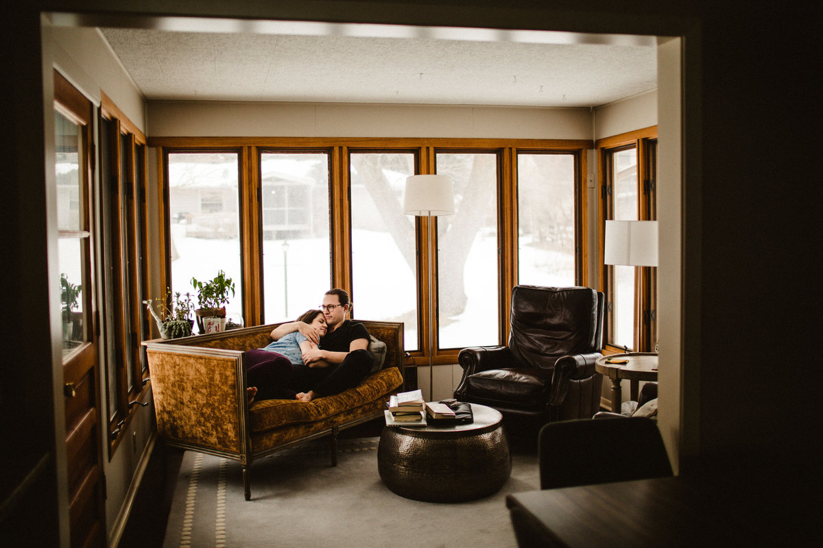 husband and wife snuggle on couch in sunroom