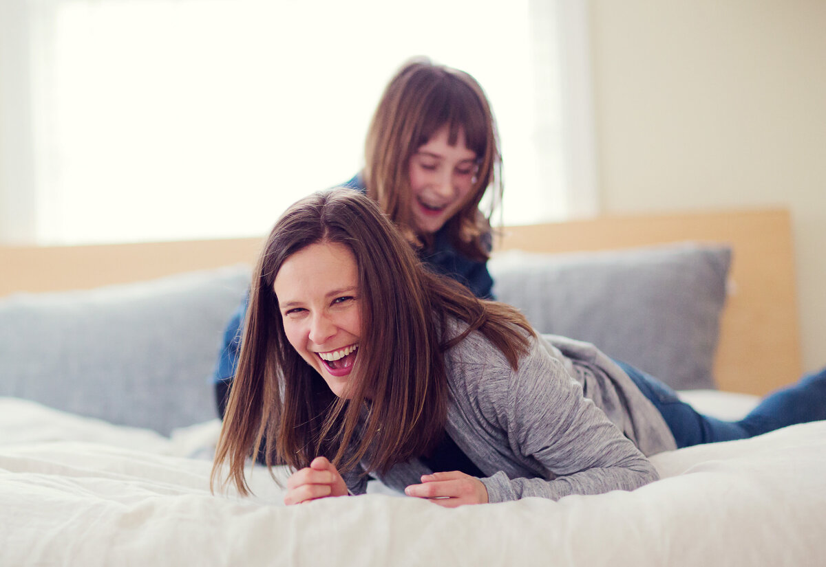 Mom is cracking up laughing while her daughter is tickling her.
