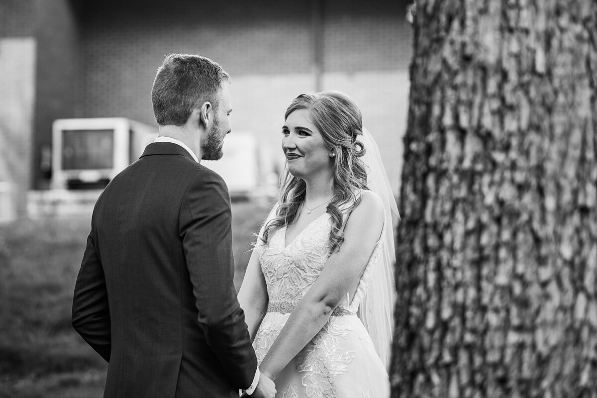 black and white image of wedding couple looking at each other by tree