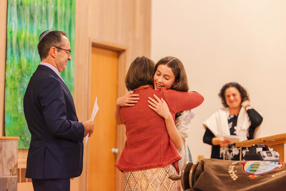 A mother in a red sweater hugs her daughter on the altar during her mitzvah