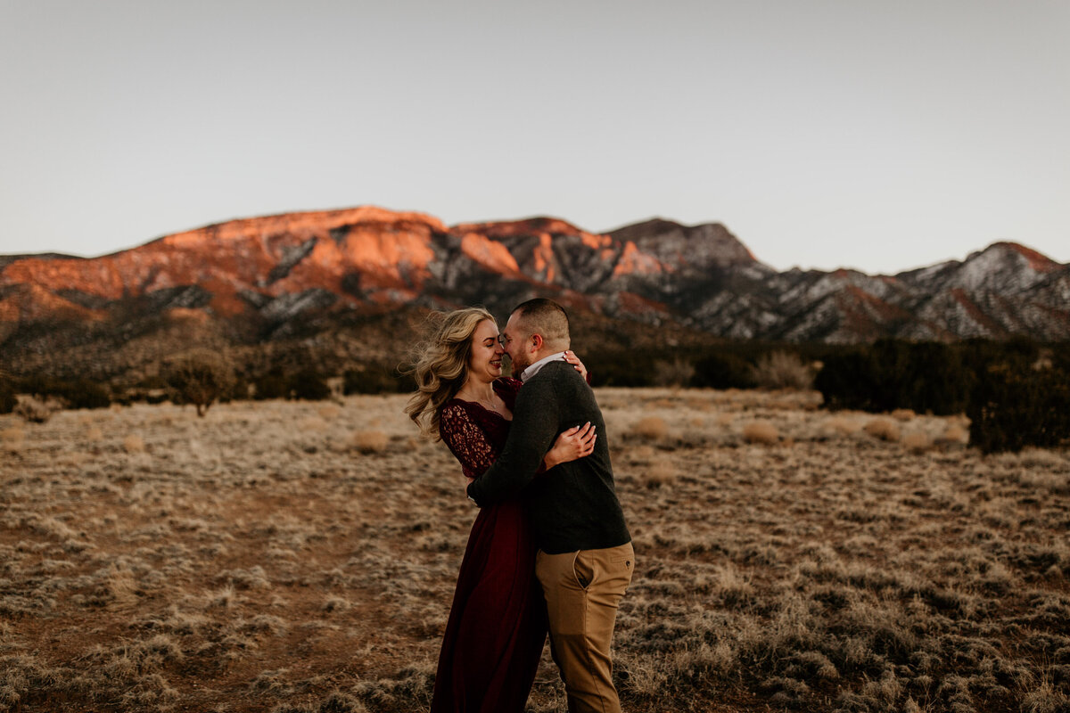 Engaged couple walking in the Albuquerque desert with the mountain behind them