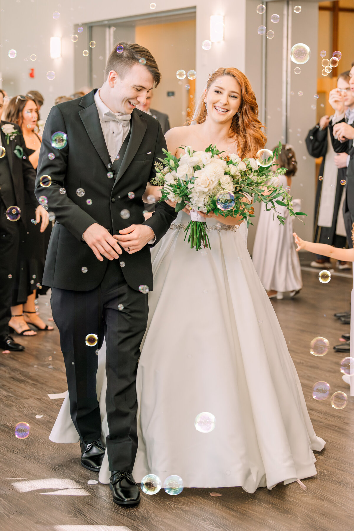A bride and groom exiting their wedding ceremony surrounded by bubbles while enjoying their Raleigh wedding photos by JoLynn Photography