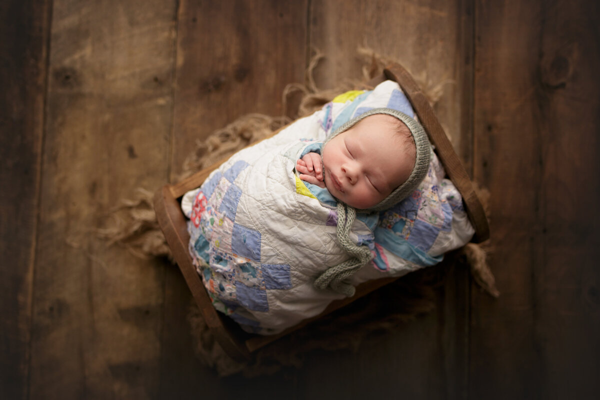 baby in cradle wrapped in blue quilt