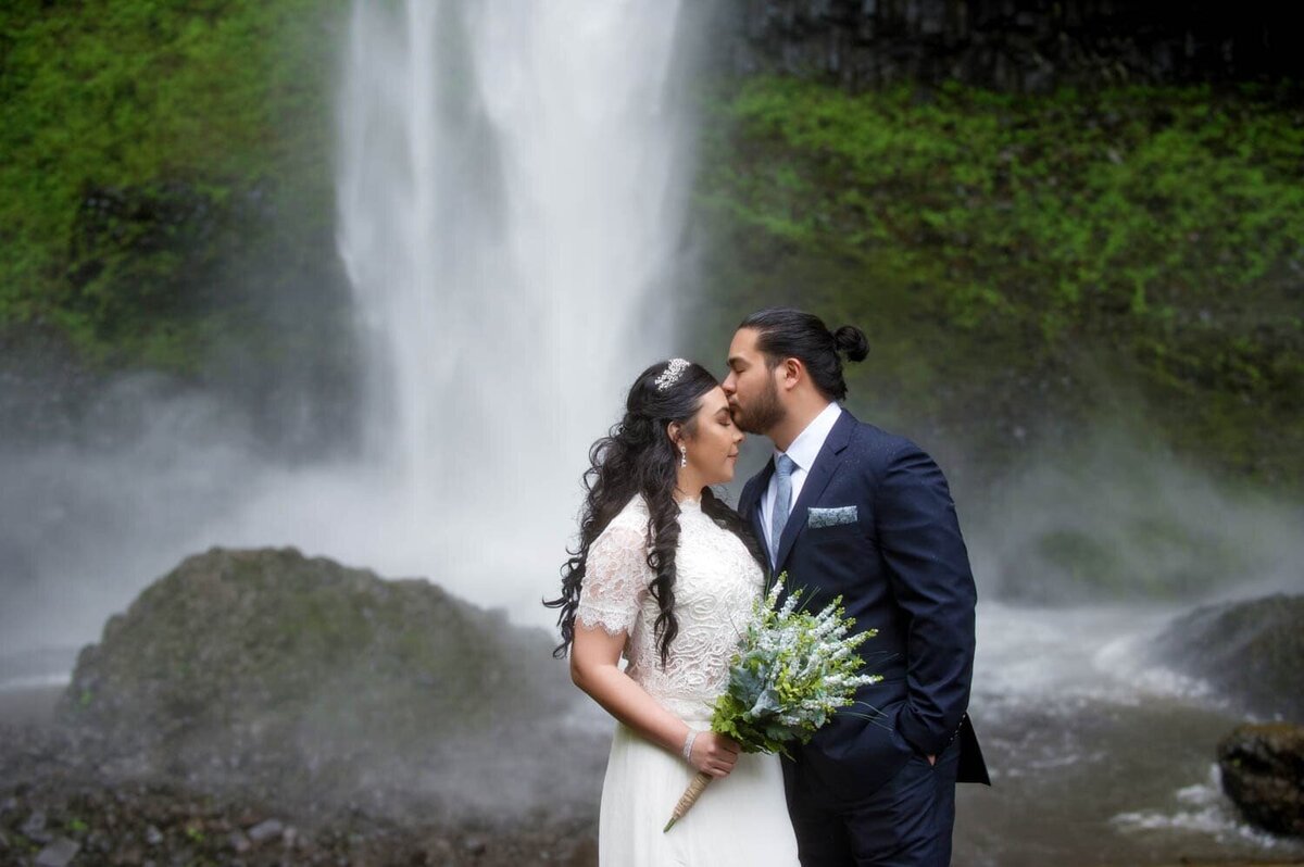 a bride and groom kiss standing in front of latourell falls