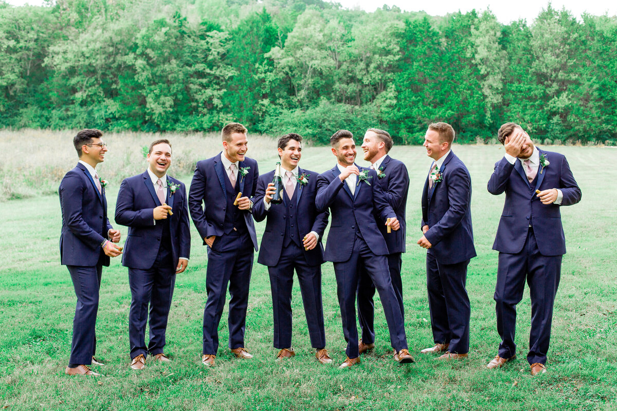 Groom with groomsmen smoking cigars outside in an open grass knoll
