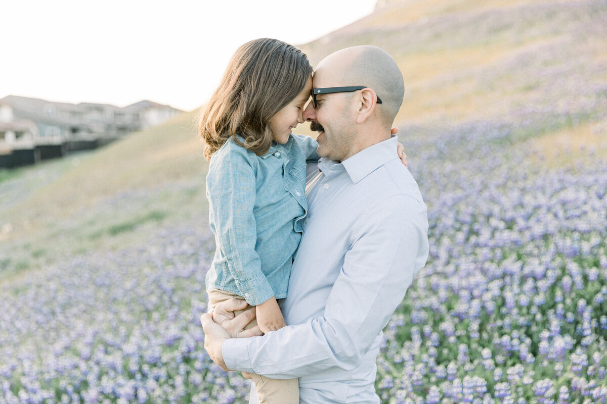Father and son standing in flower field pressing foreheads together taken by Newborn Photographer Sacramento Kelsey Krall