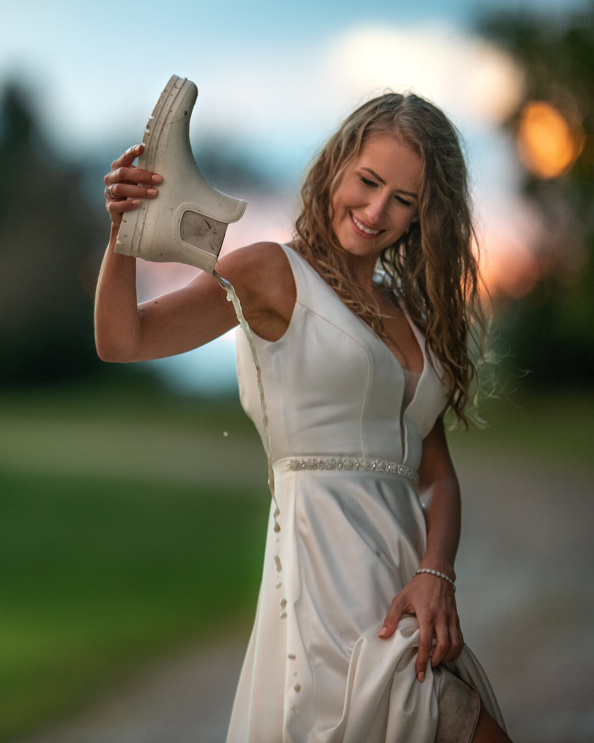 Bride in wet and muddy wedding dress dumping water from her white rain boots