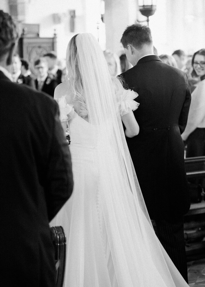blurry black and white photo father and daughter walking down the aisle at church wedding