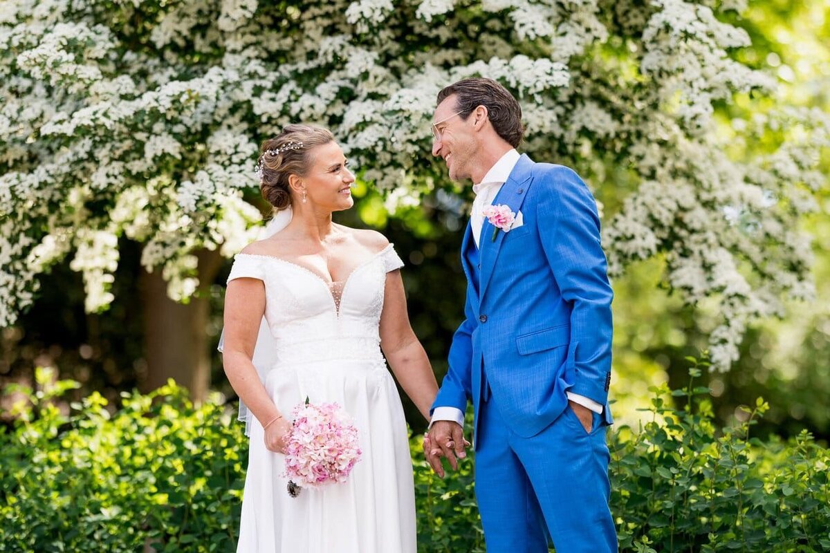 Bruidspaar loopt hand in hand, de bruid draagt een prachtig roze trouwboeket, professioneel begeleid door weddingplanner