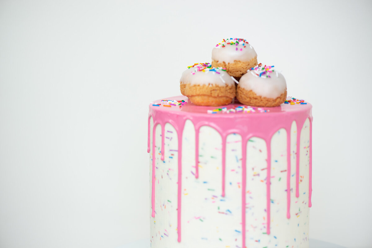 White single tier drip wedding cake with sprinkles, topped with pink drizzle glaze and sprinkled cream puffs, created by Crème Cream Puffs, playful and modern cakes & desserts in Calgary, Alberta, featured on the Brontë Bride Vendor Guide.