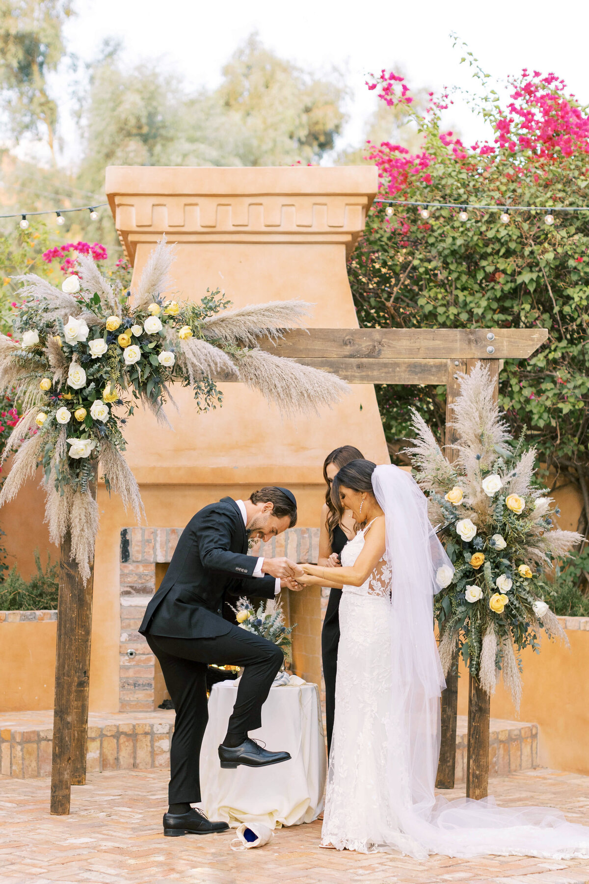 Bride and groom holding hands while the groom breaks the glass carefully wrapped with white cloth at this southern california wedding