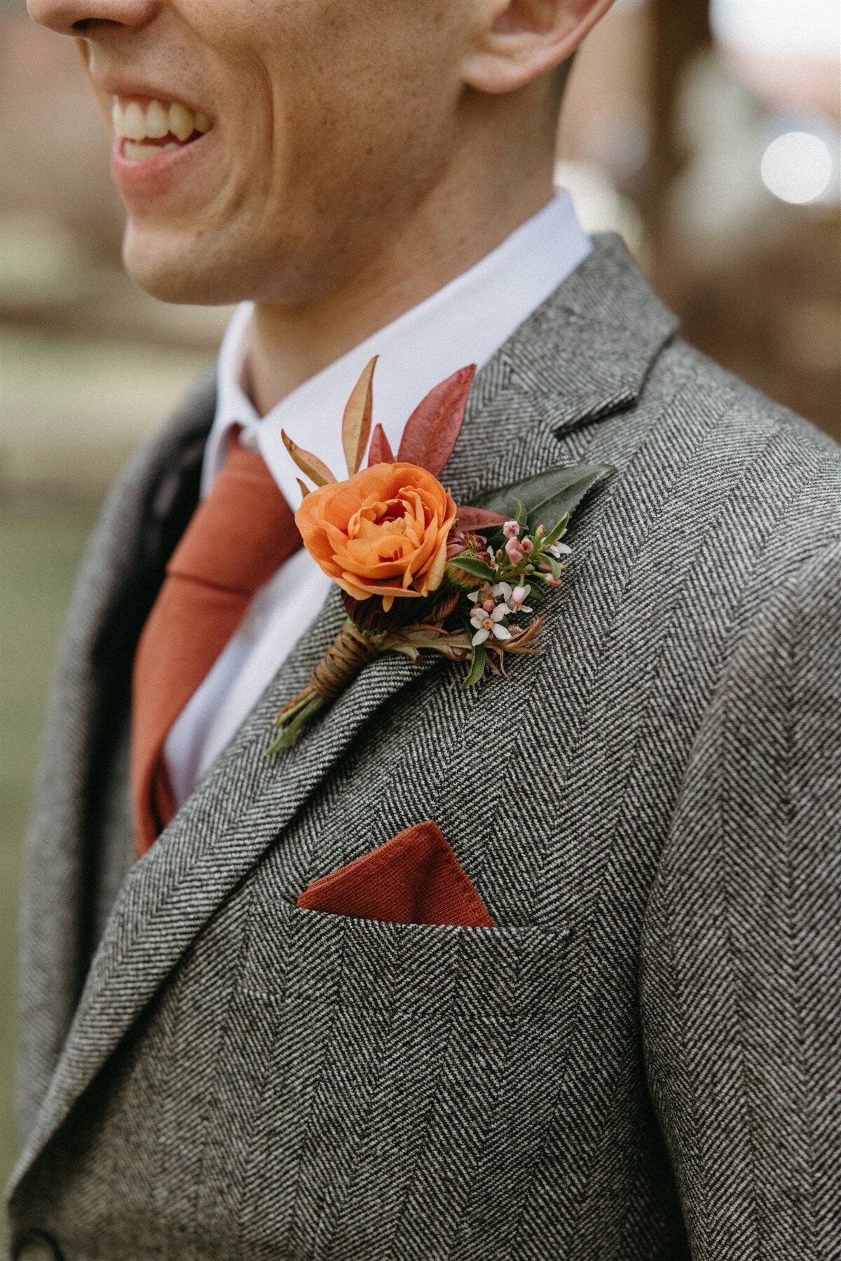 Groom wearing grey suit with orange flower boutonniere