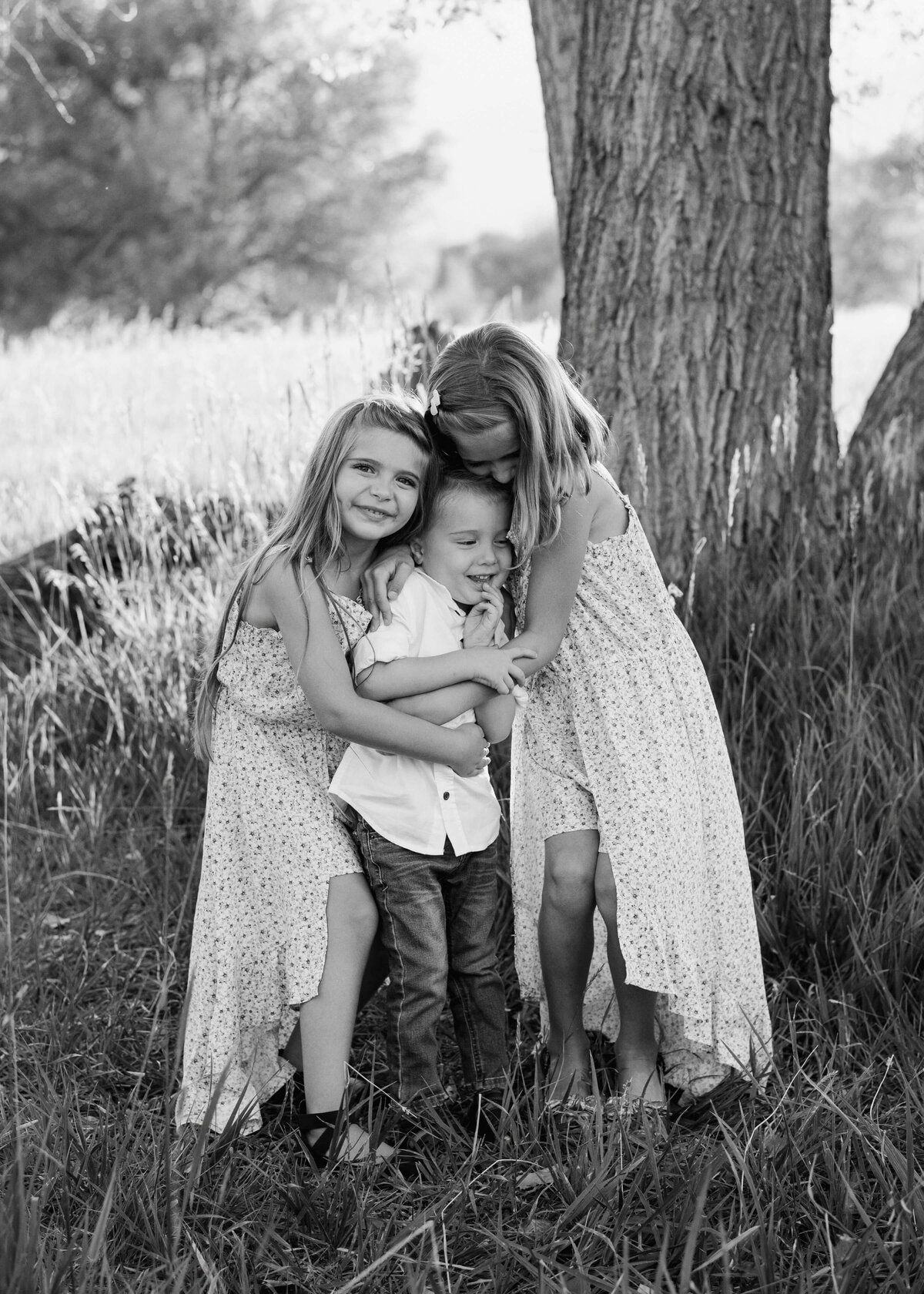 Two young girls hug their toddler brother in a black and white image