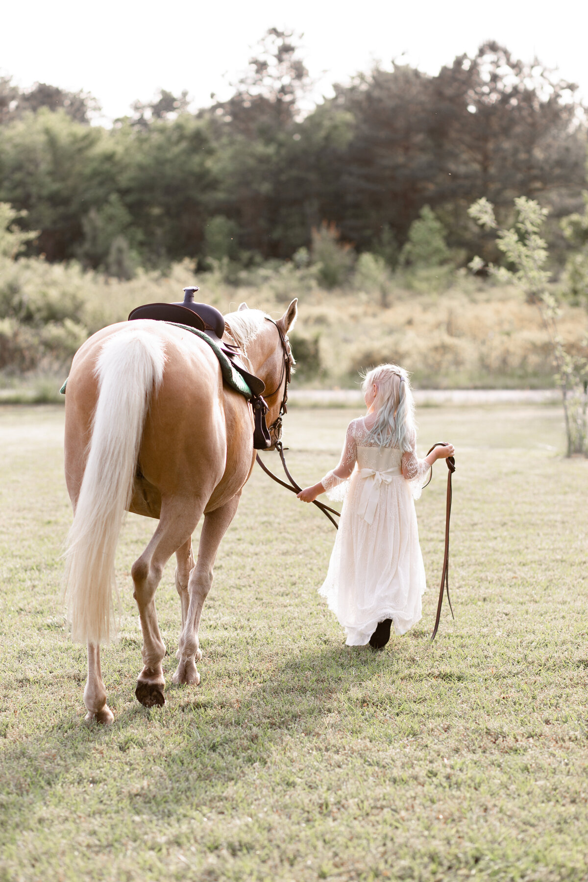 a girl in a white dress walks her horse through feild