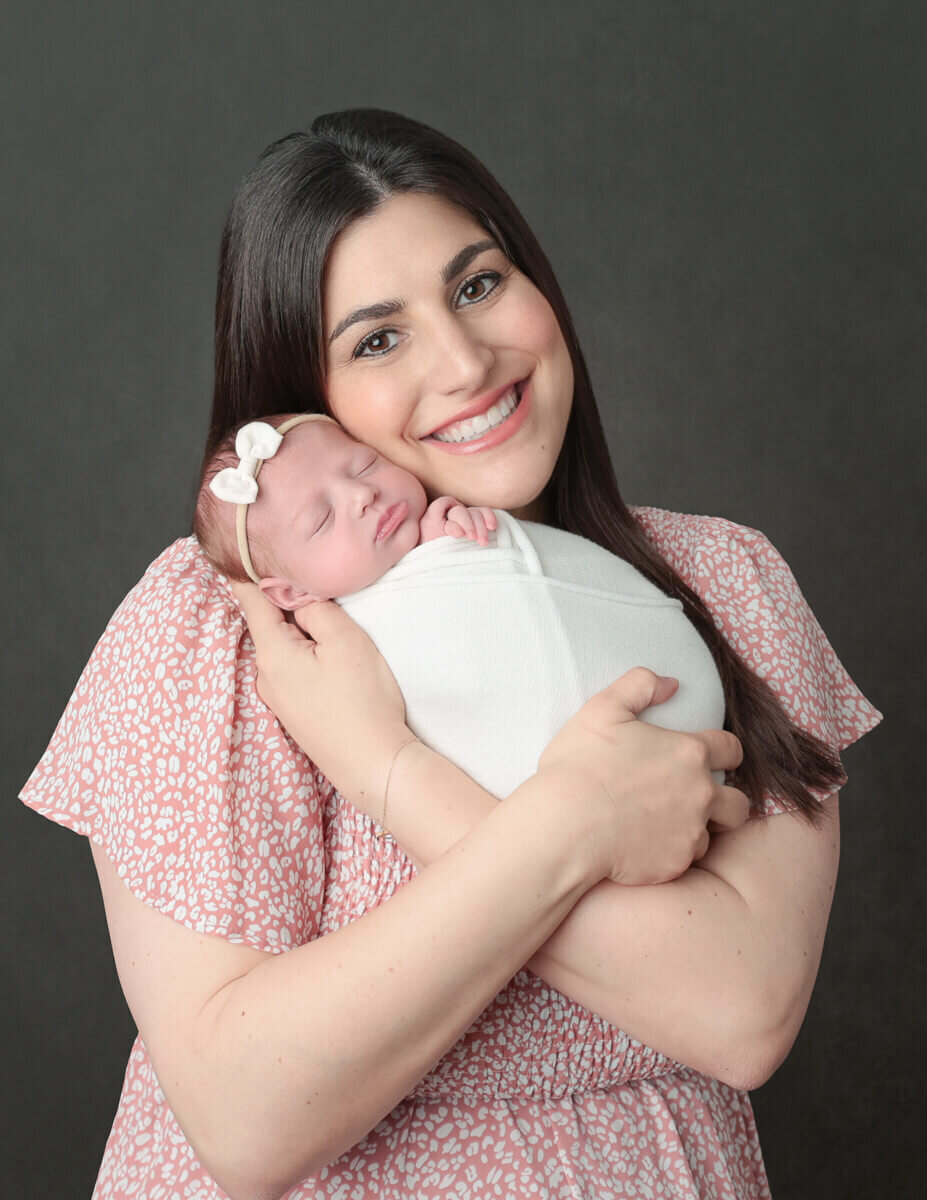 A tender moment captured in a photography studio in Rochester, NY, featuring a newborn peacefully nestled in their mother's arms.