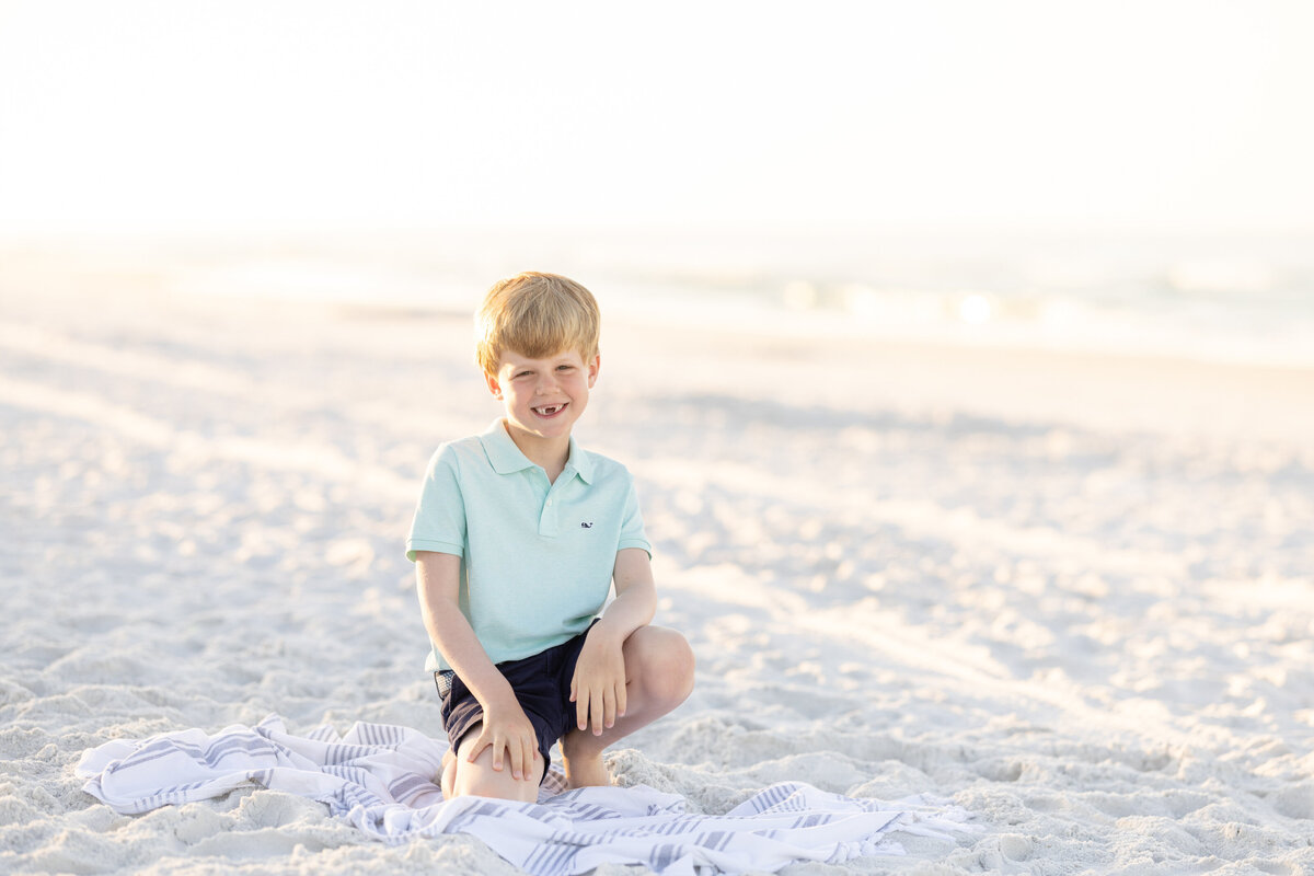 A young boy kneeling down in the sand at the beach