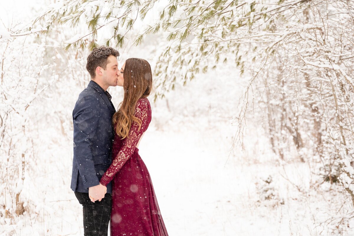 Couple-dresses-up-for-their-engagment-session-and-share-a-kiss-as-the-snow-falls-during-their-winter-engagement-session-at-Sydenham-ridge