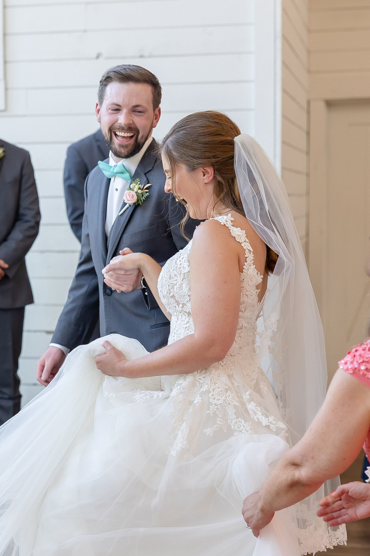 groom laughs as he leads bride up the step at indoor Morgan Creek Barn wedding ceremony in Dripping Springs