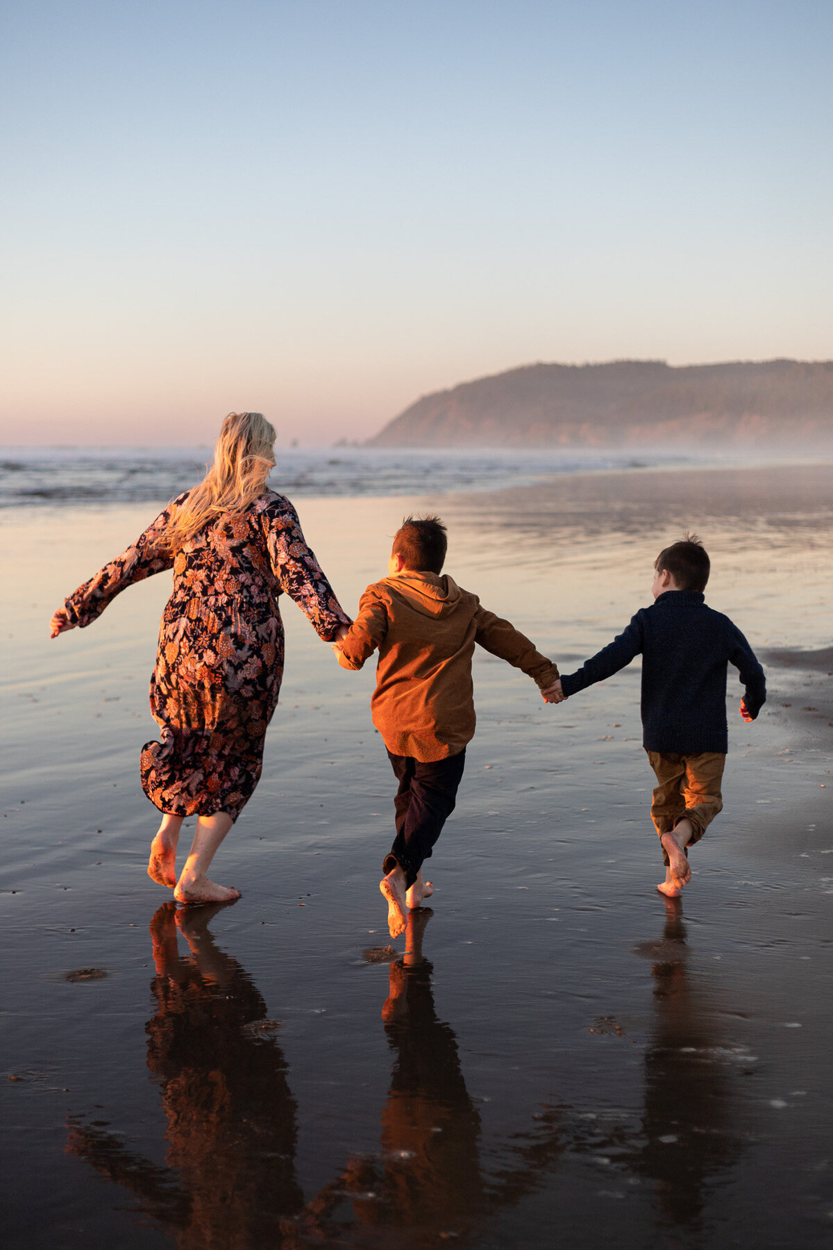 Mother and sons running on Cannon Beach at sunset.