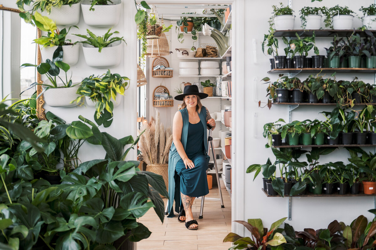 Woman sitting on a ladder in a plant store looking out the window
