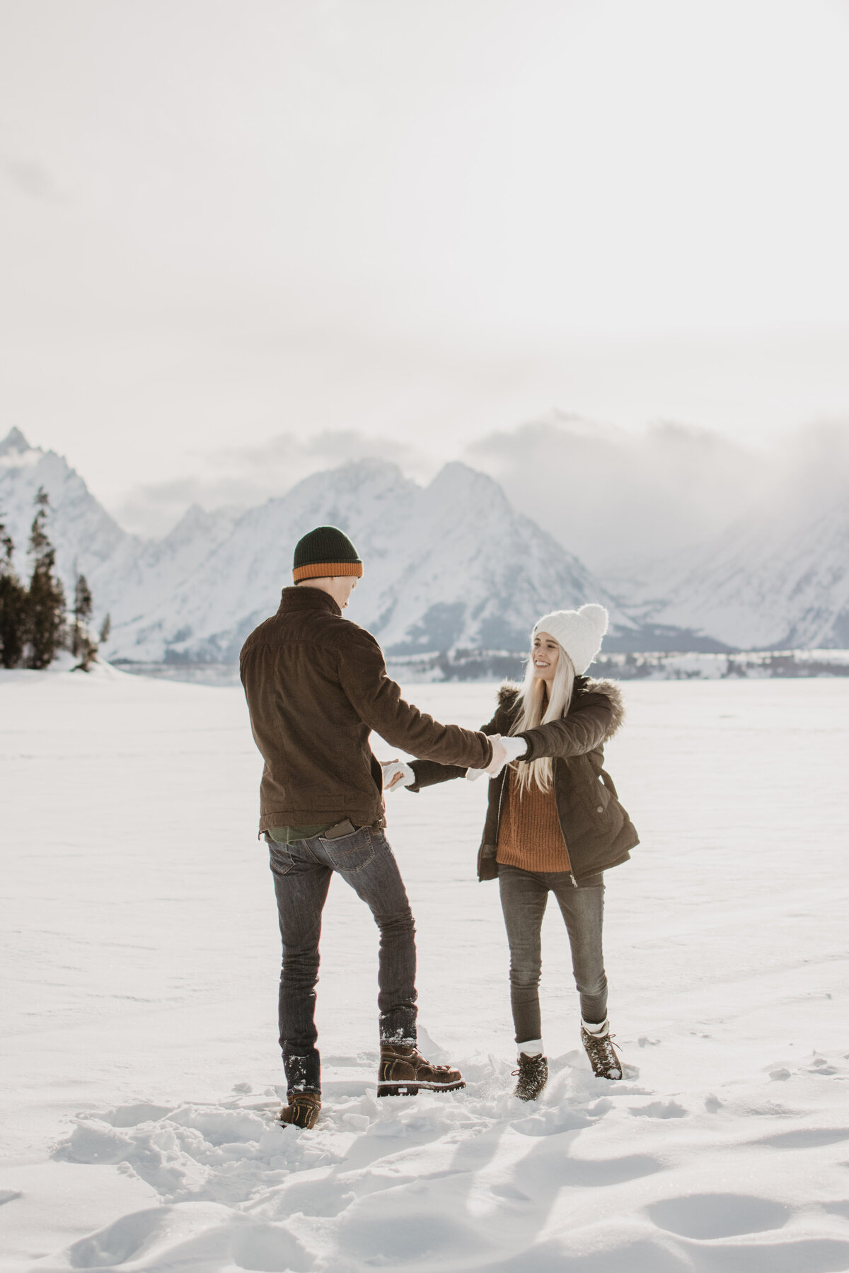 engaged couple in their Jackson Hole engagement session dancing in the snow and holding hands captured by jackson hole photographers