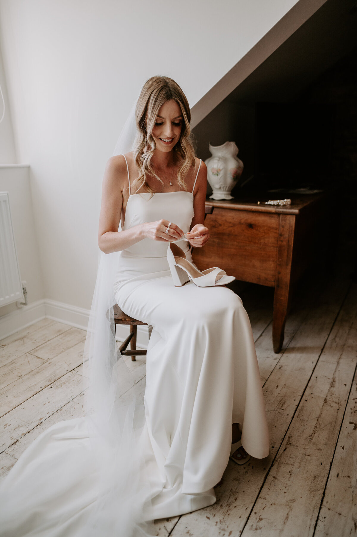 A brides sits in her wedding dress ready to put on her shoes in the Bridal prep suite at Anran // Tidwell Farm in Devon.