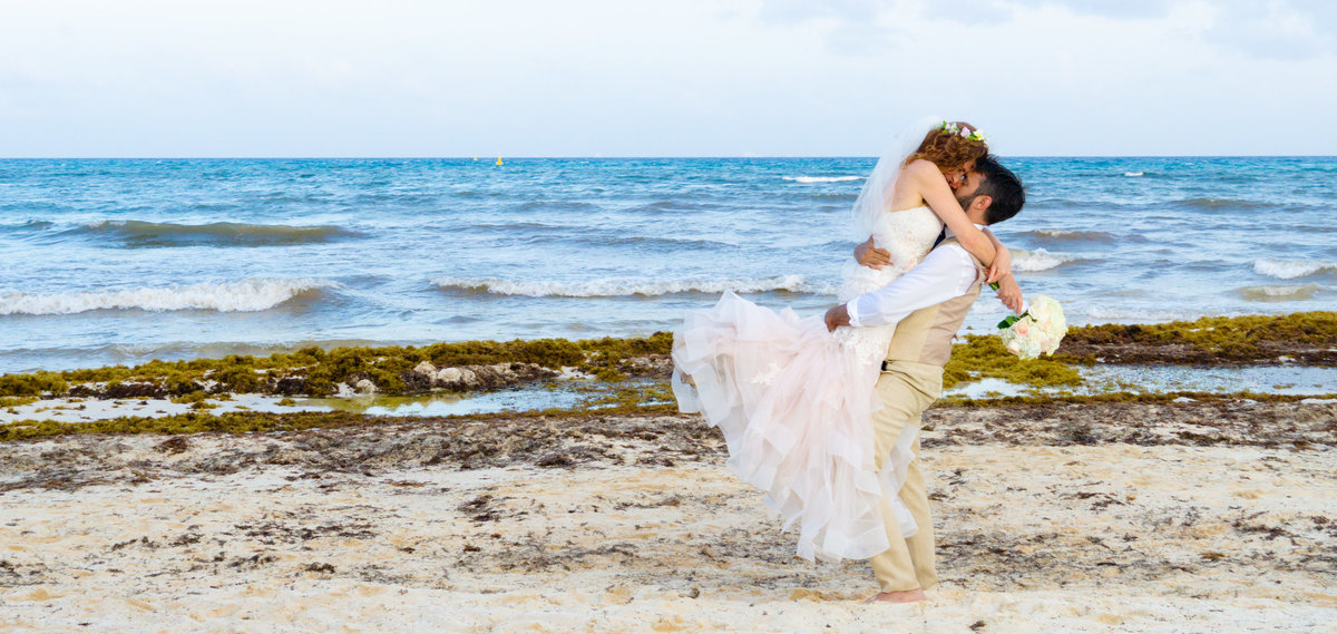 Groom holding and kissing bride in front of the ocean in Mexico