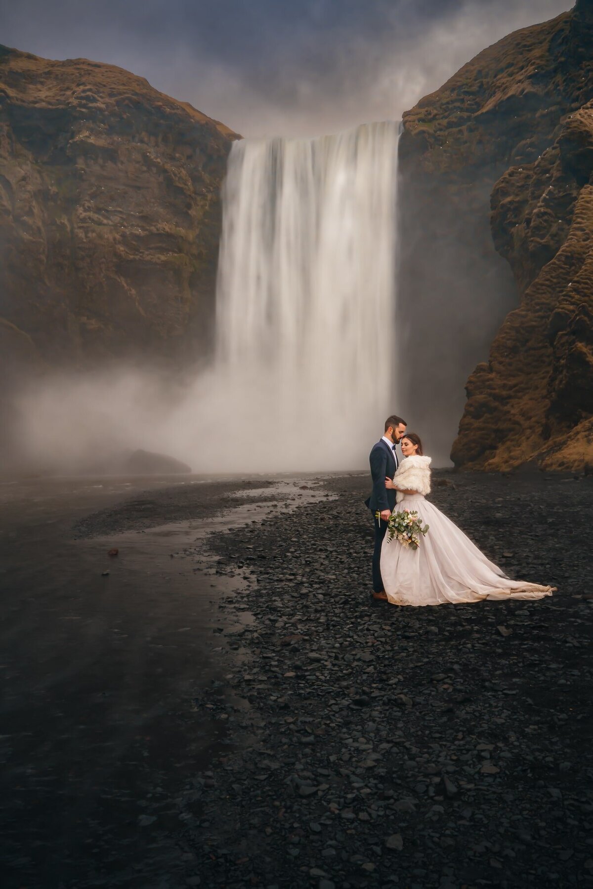 This couple shares a special moment in front of the breathtaking Skogafoss waterfall in Iceland, capturing the essence of their love amid the cascading beauty.