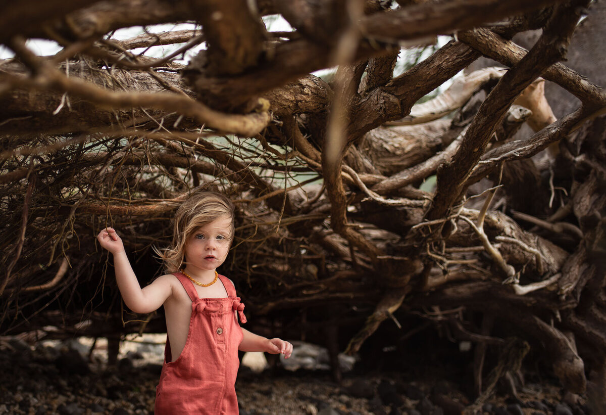 girl looking at camera under tree roots with hair blowing at saint louis family photography session