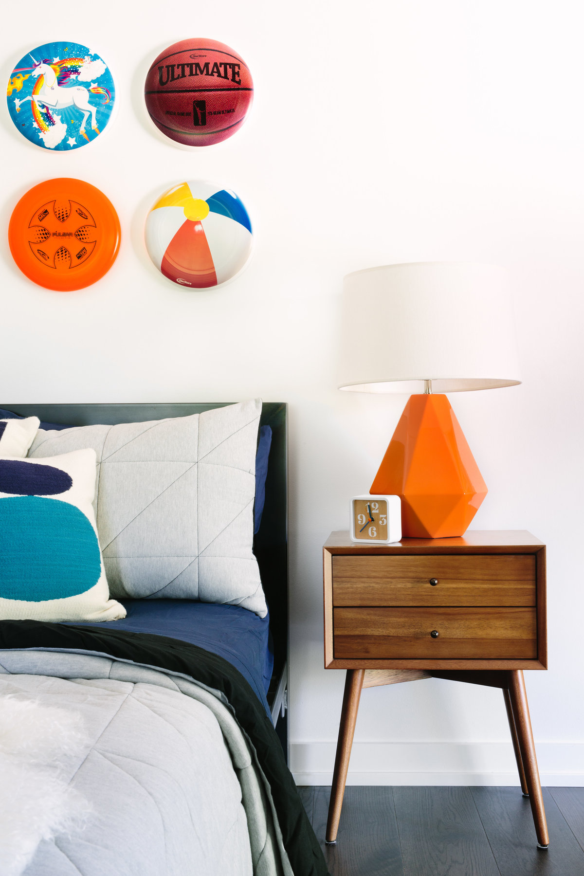 Boys bedroom with walnut nightstand, orange lamp, and frisbee art installation