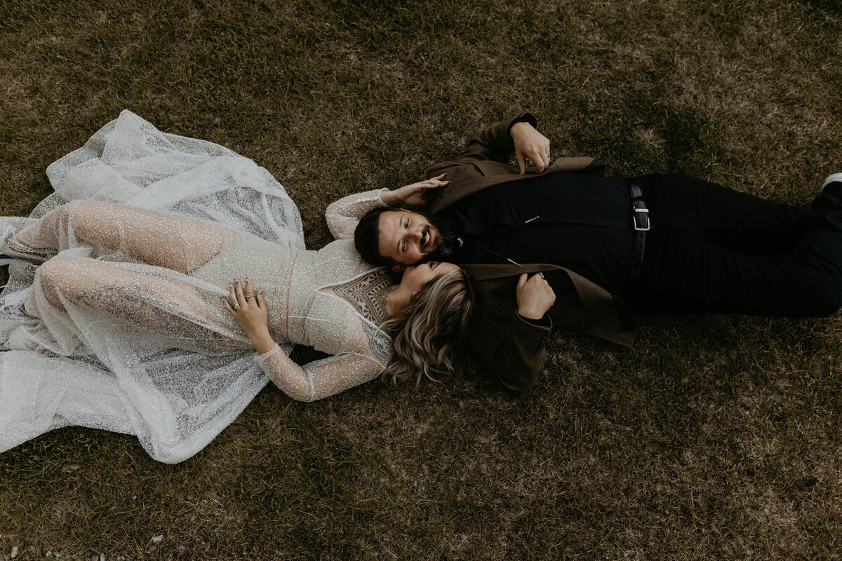 bride and groom laying together in grass wearing their wedding attire