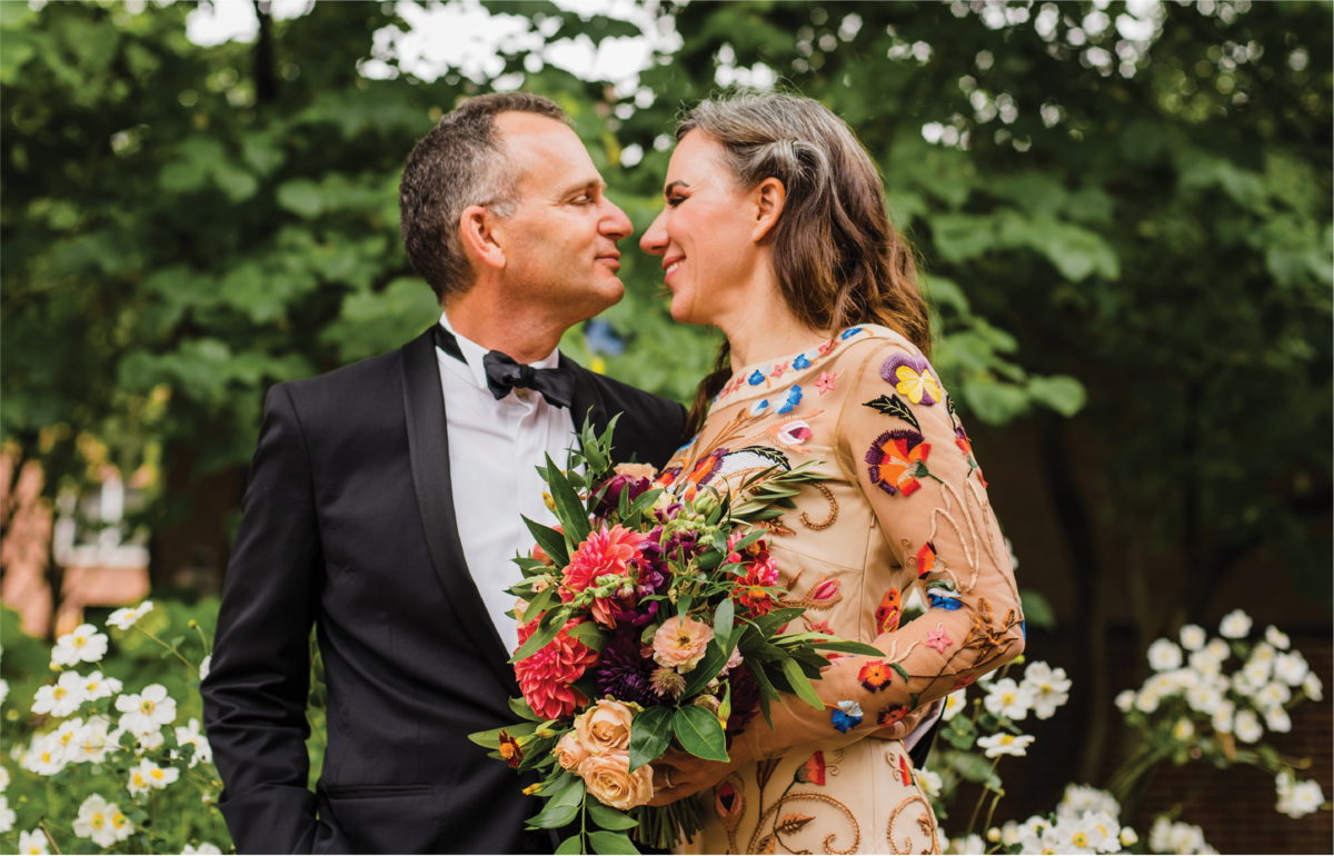 Bride and Groom in a Floral Gown and Black Tuxedo staring into each other’s eyes outdoors.