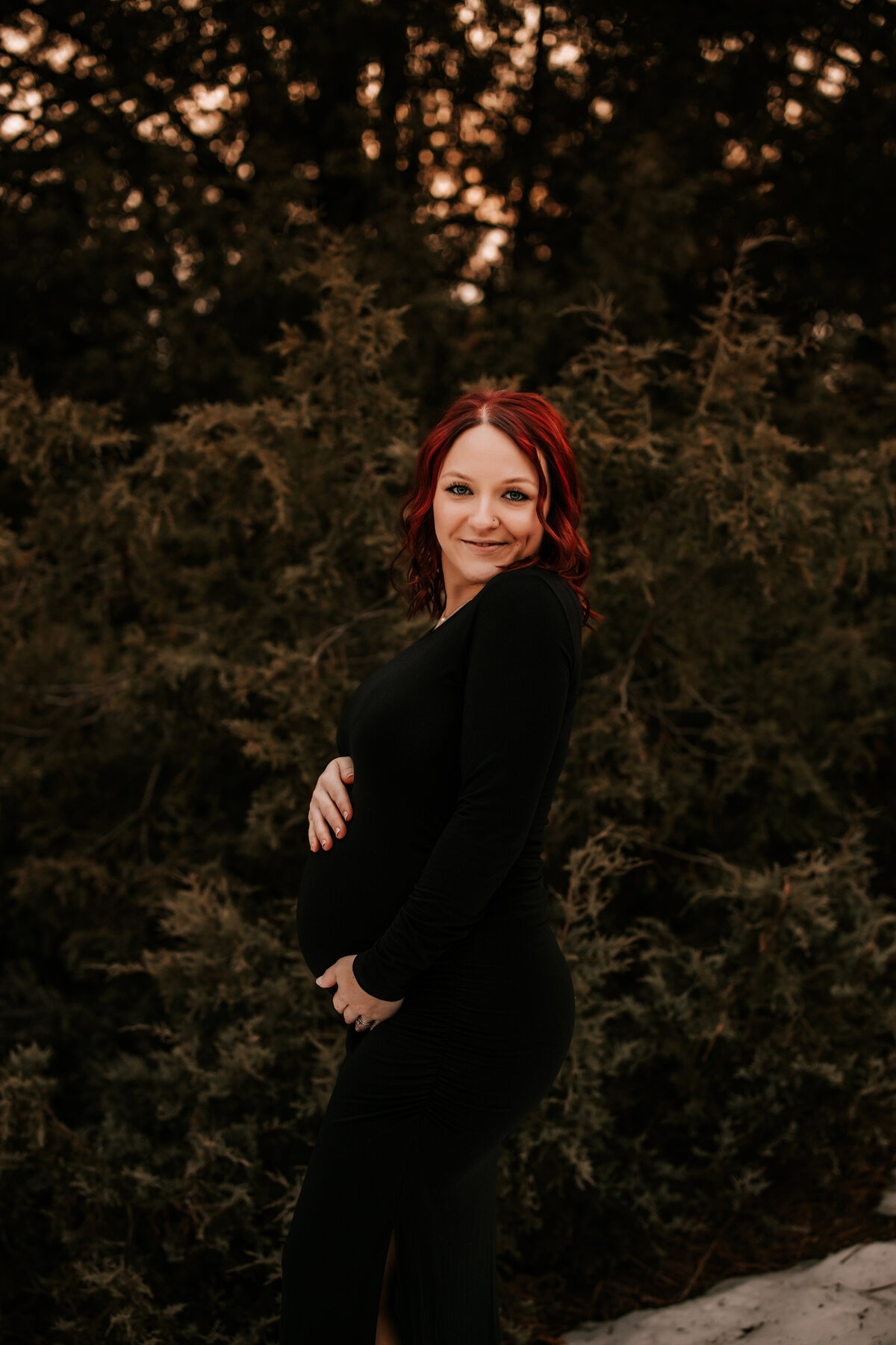 pregnant mom wears tight black dress in a snow forrest in colorado