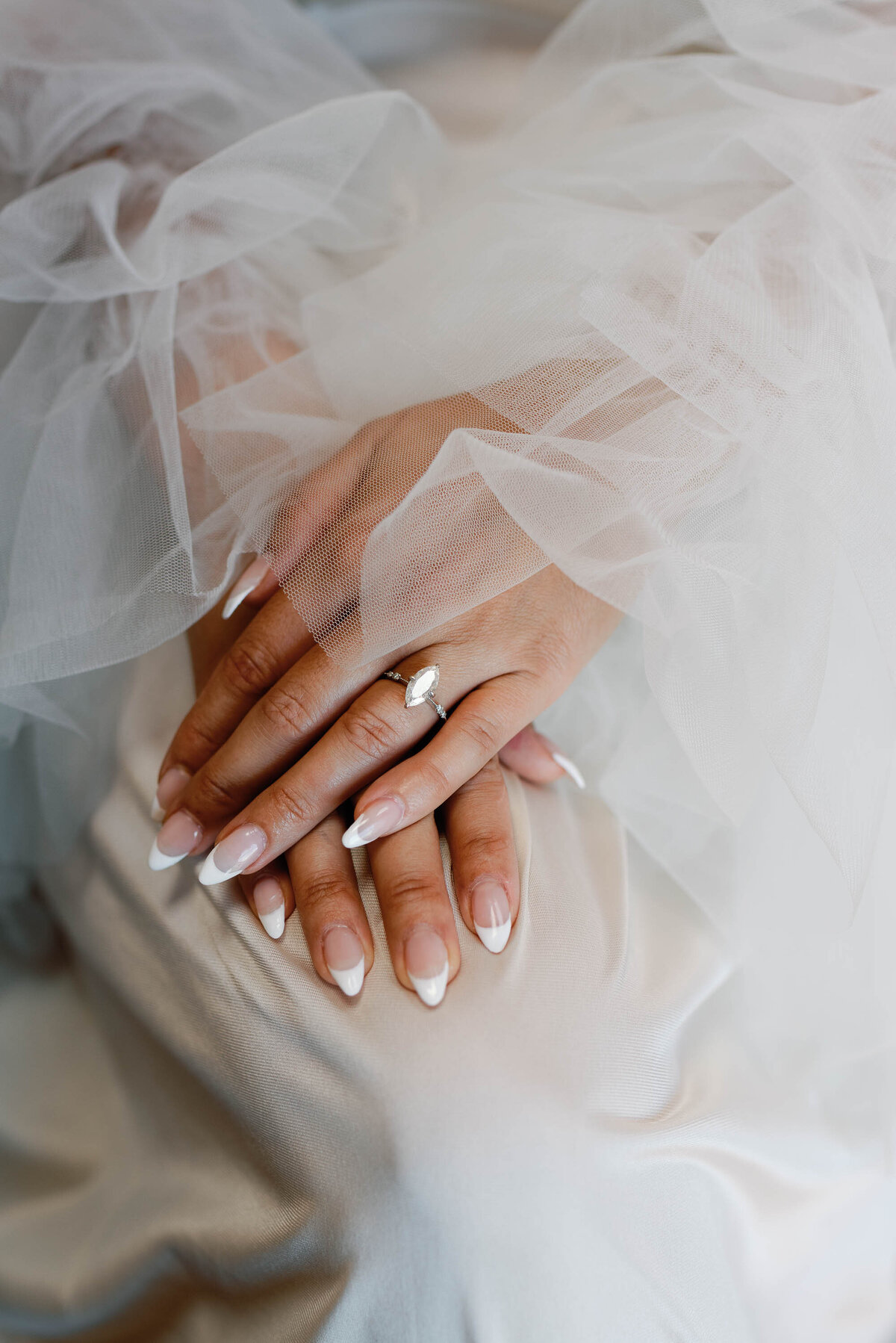 close up of bride rests hands with tule surrounding baquette ring