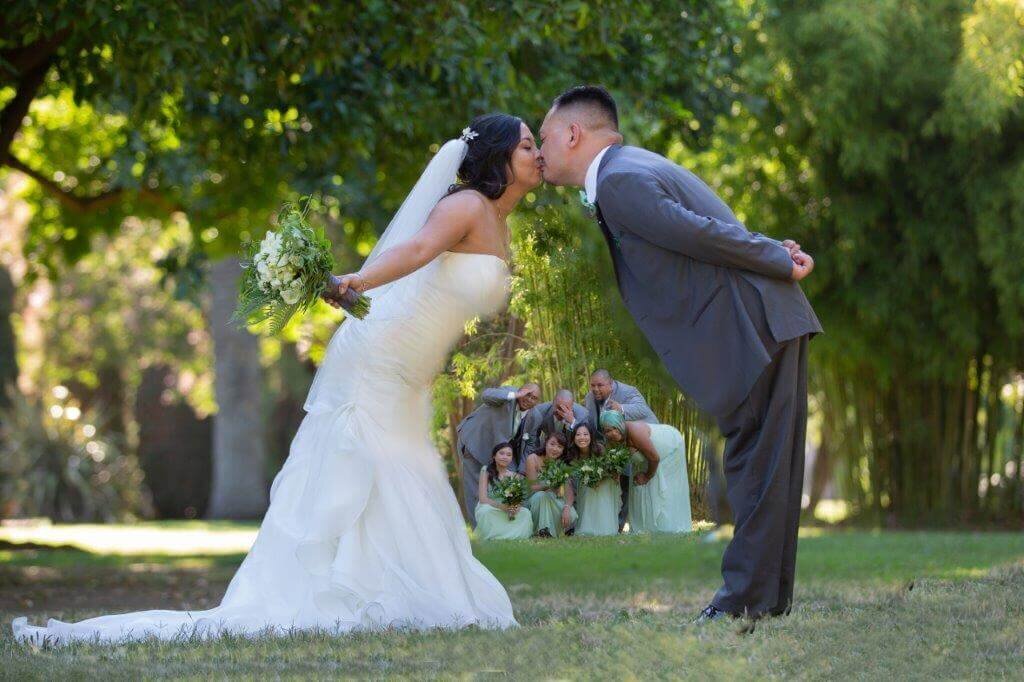 Bride and groom kiss with their wedding part in the middle of them looking on with excitement and humor. Captured and edited by sacramento wedding photography studio philippe studio pro.
