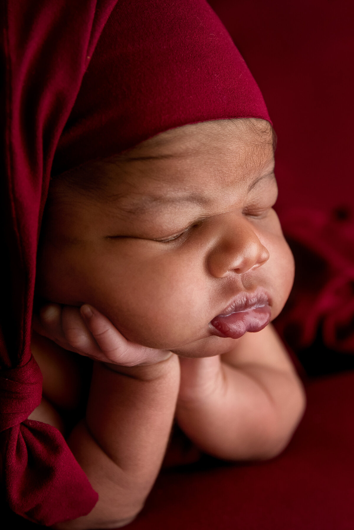 st-louis-newborn-photographer-sleeping-newborn-baby-holding-head-with-monocramatic-red-cap-and-background