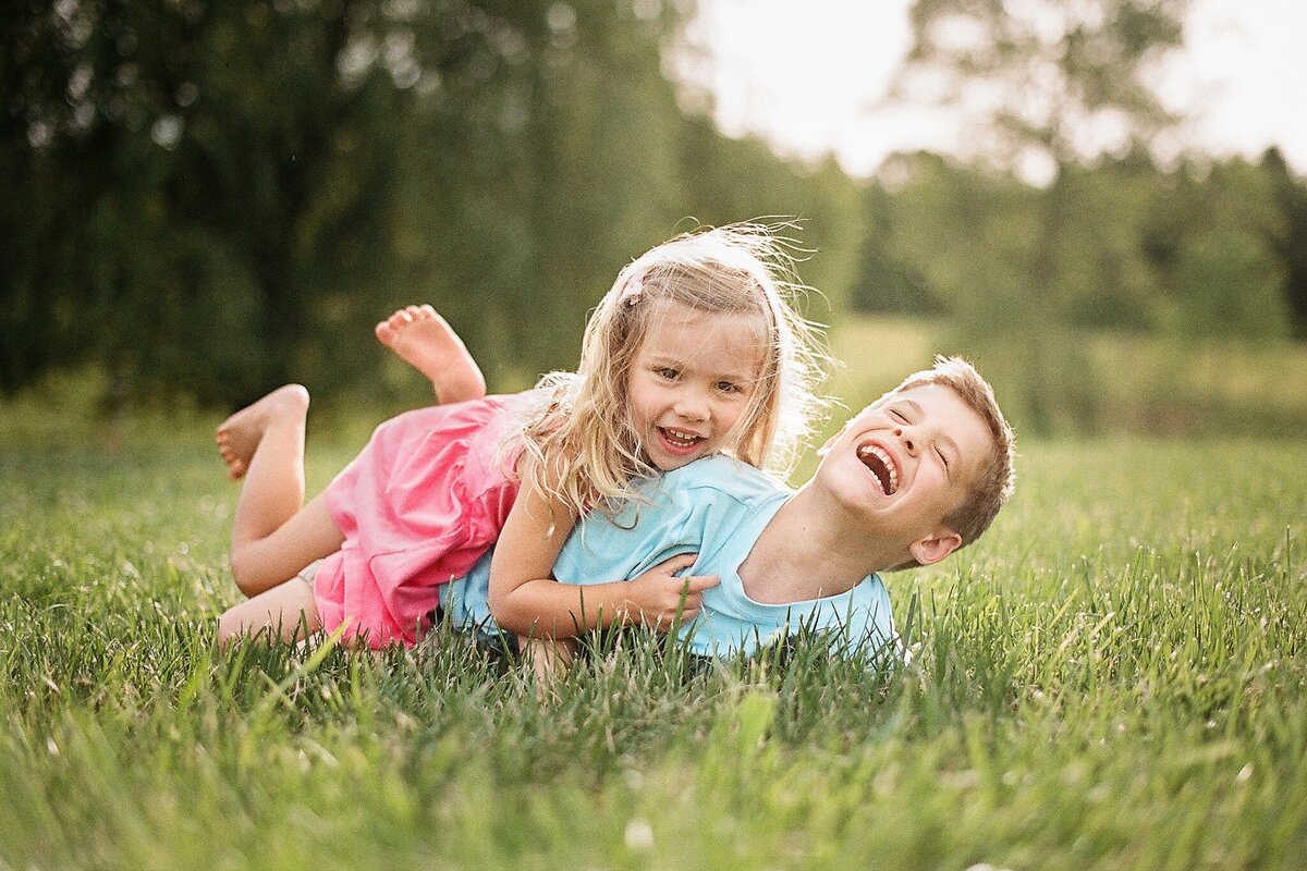 spring image of brother and sister wrestling and laughing in grass