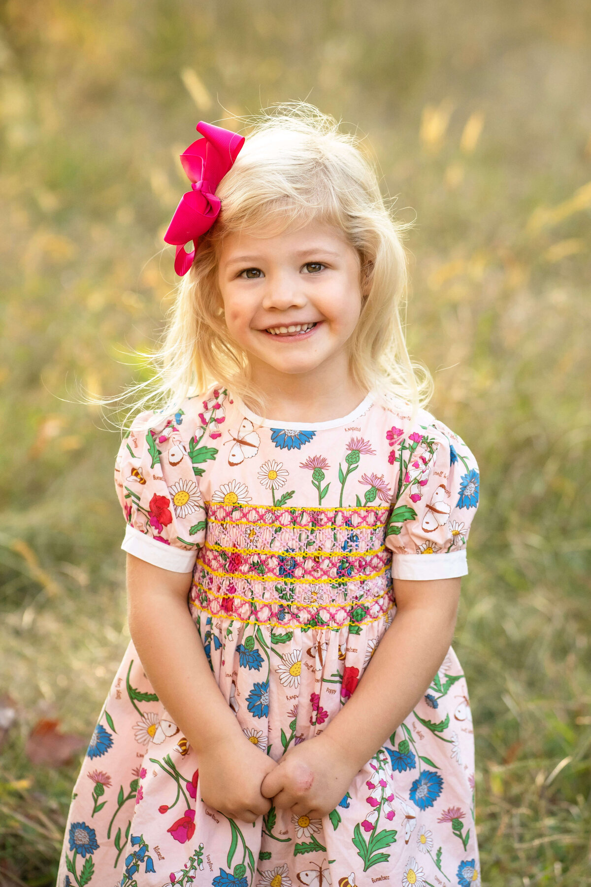 3 year old blond girl smiling at the camera in a field