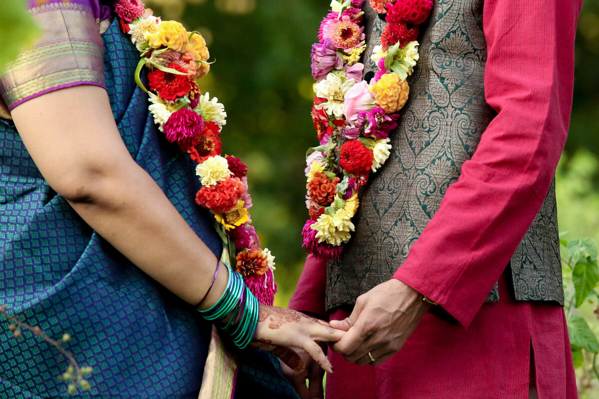 Detail shot of Hindi bride and groom facing each other touching hands wearing colorful garlands and henna tattoos New York wedding Photographer